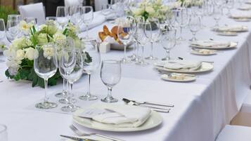 Una larga mesa de comedor dispuesta para un evento formal, con manteles blancos, cristalería y centros de mesa florales.