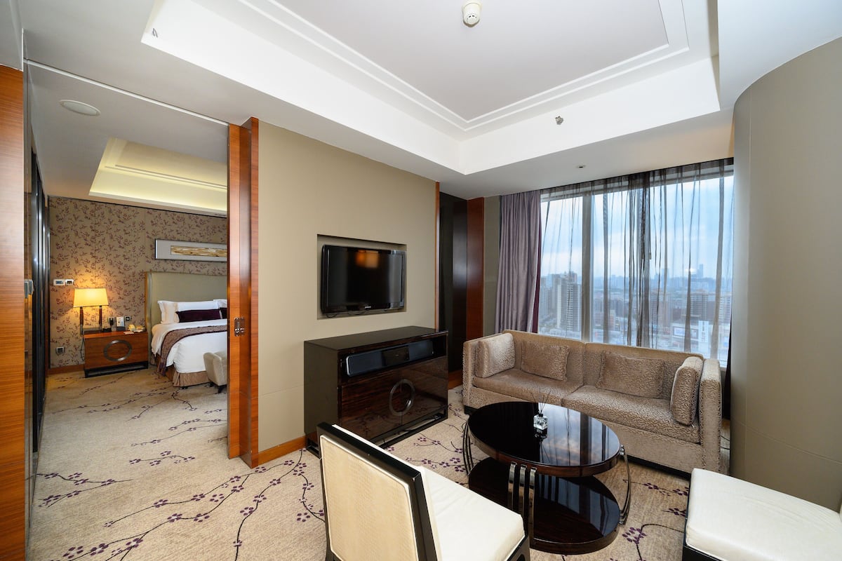 A hotel room with a bed, a TV, a sofa, a coffee table, and a view of the city.