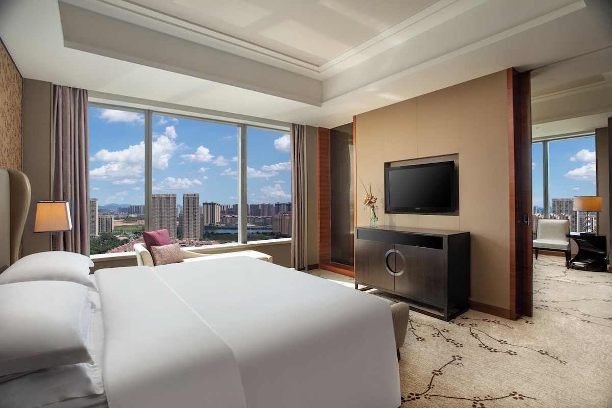 Habitación de hotel con una cama grande, televisión de pantalla plana, escritorio y vista a la ciudad.