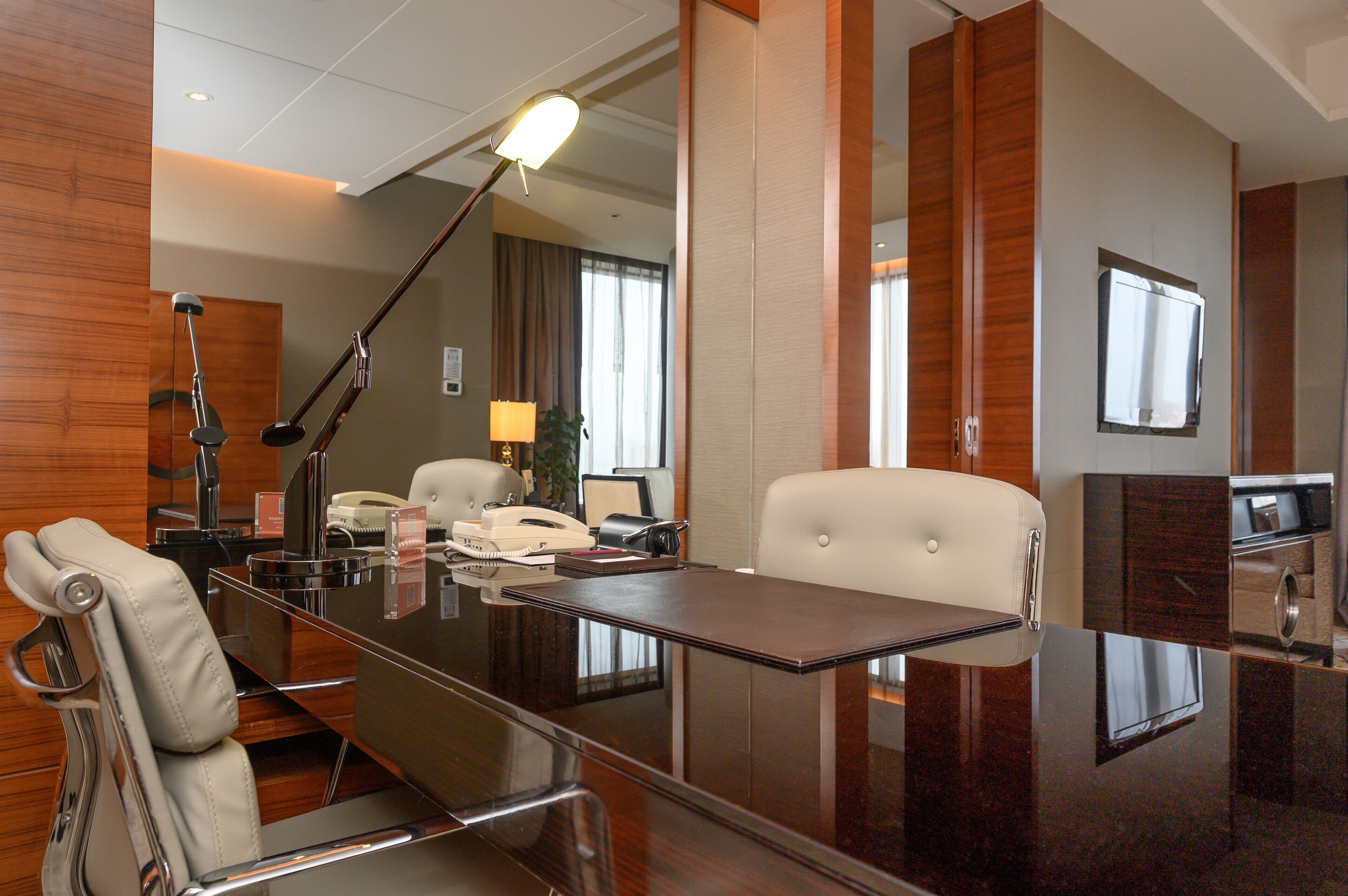 A modern hotel room with a large desk, a chair, a lamp, a telephone, and a television.