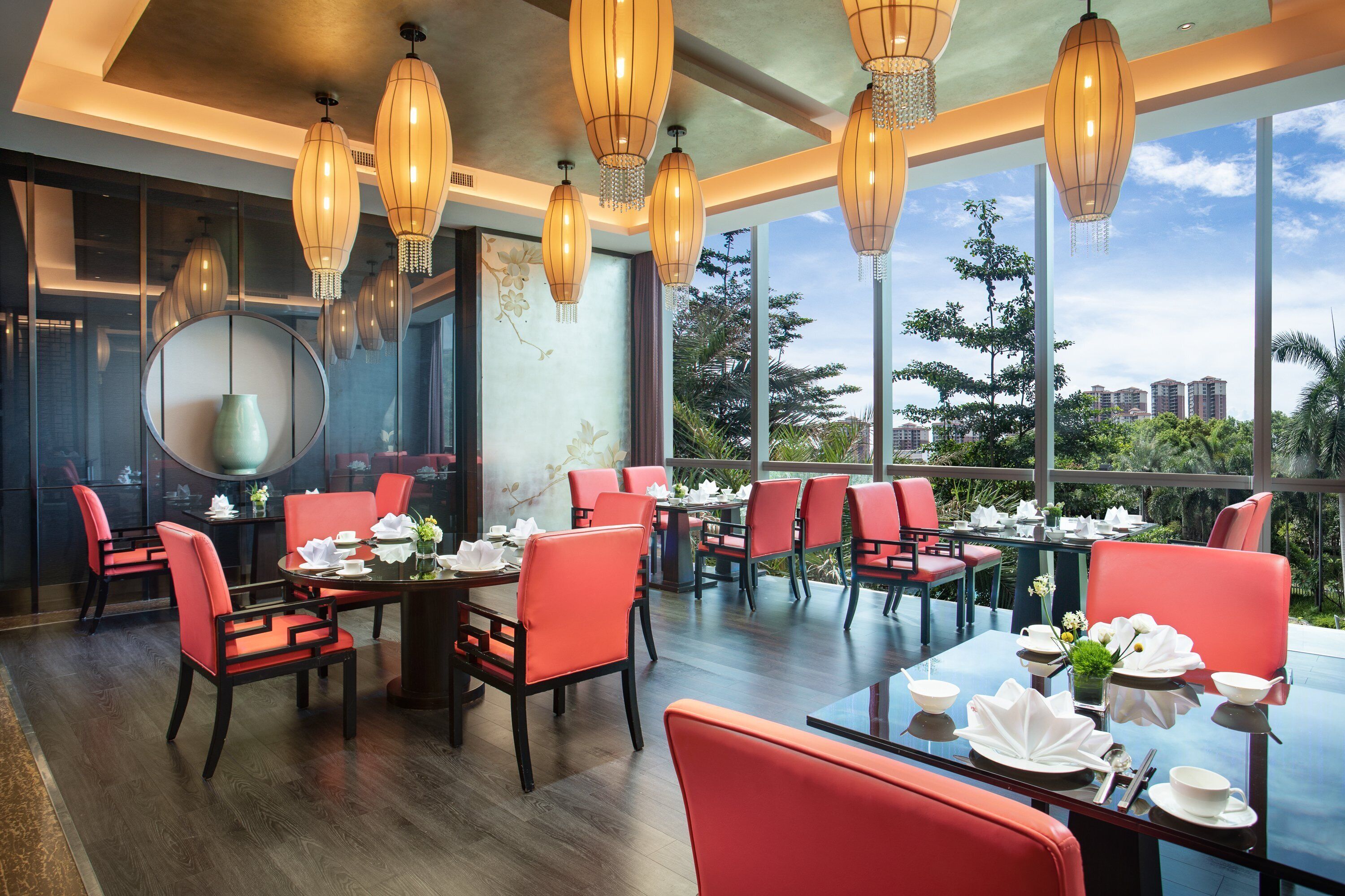 A restaurant with red chairs and tables, large windows, and hanging lanterns.