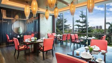 A restaurant with red chairs and tables, large windows, and hanging lanterns.