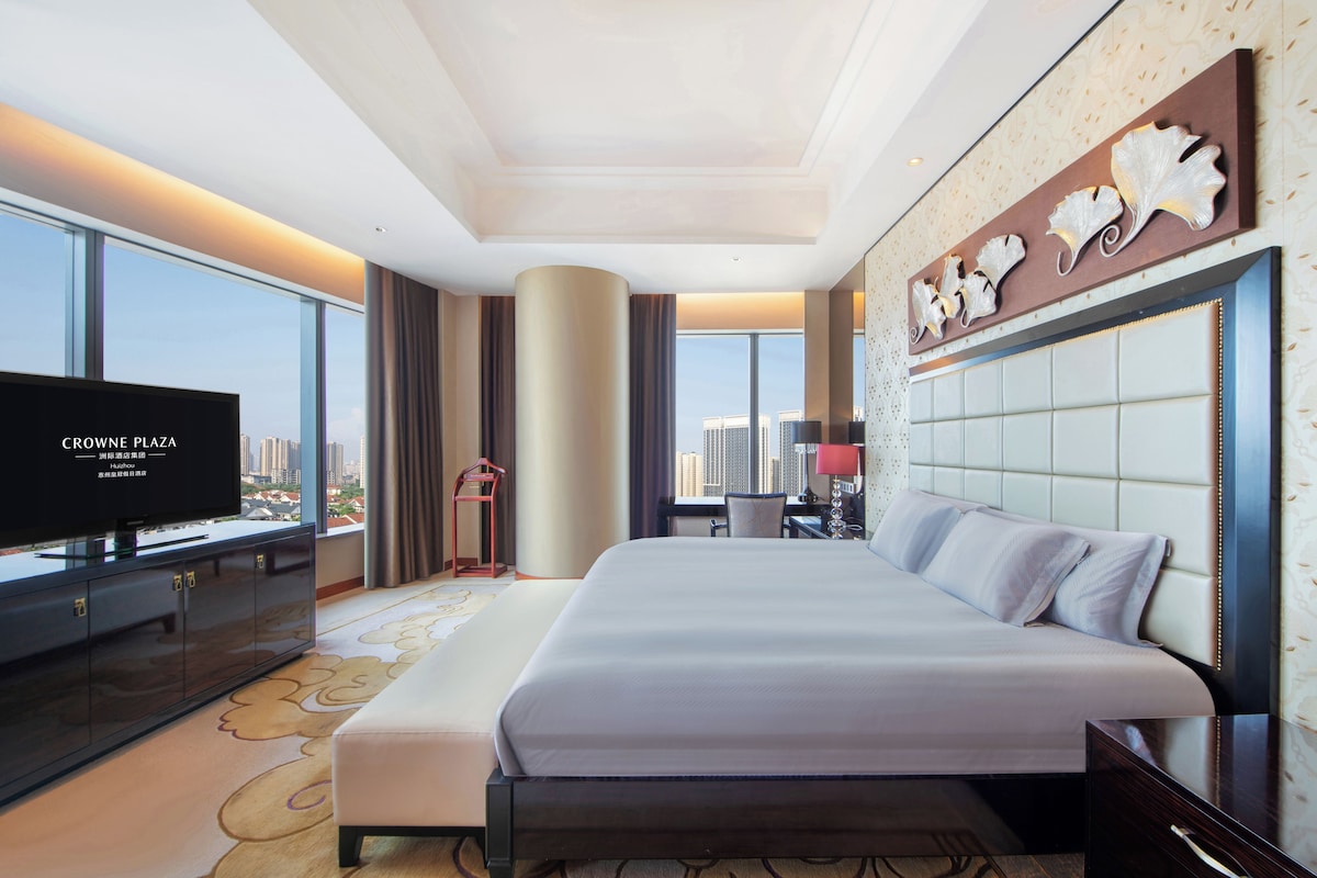 Habitación de hotel con una cama grande, televisión, escritorio y vista a la ciudad.