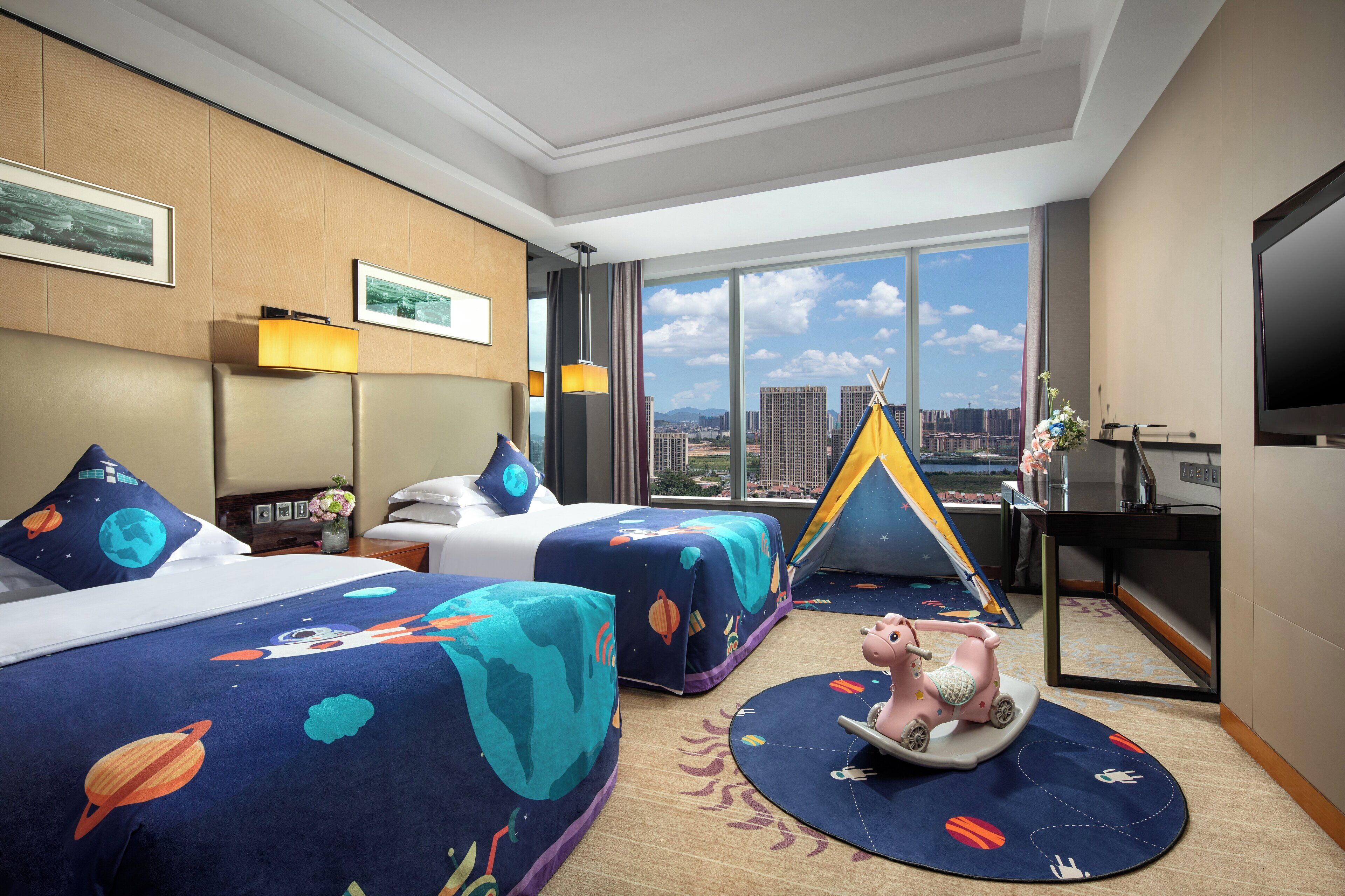 A hotel room with two beds, a desk, a TV, and a view of the city.