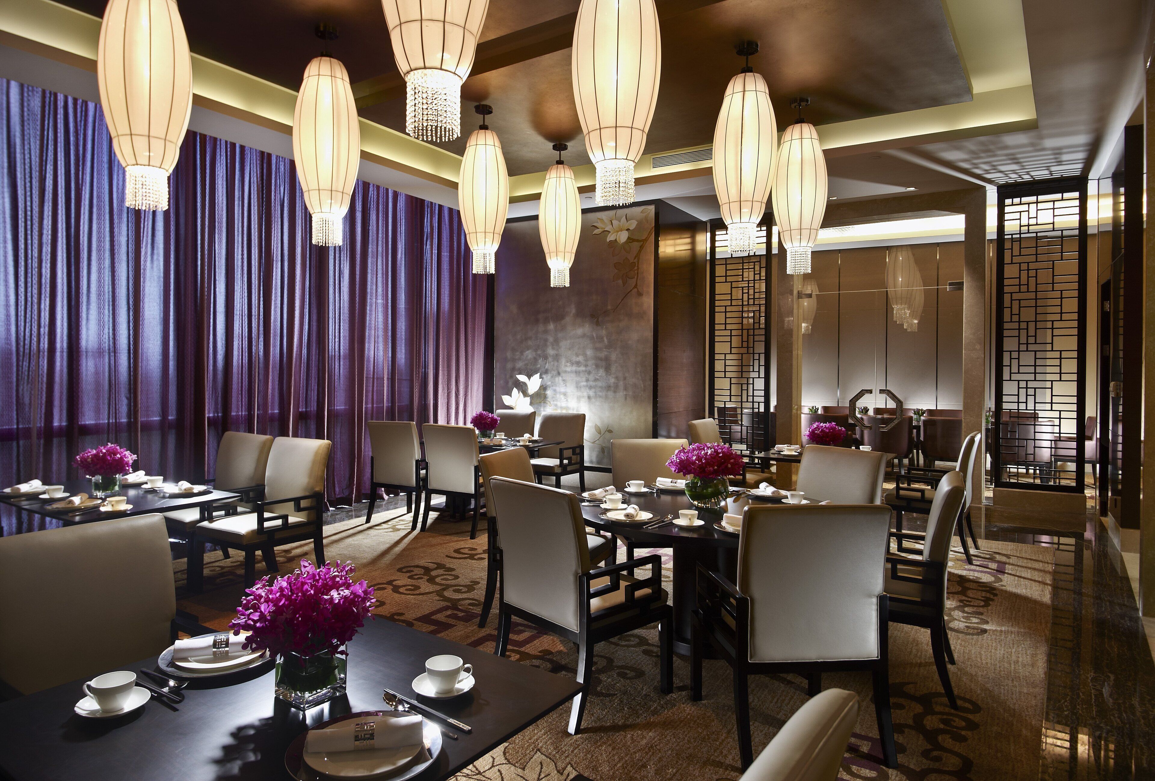 Comedor de hotel con varias mesas, sillas y candelabros colgantes.