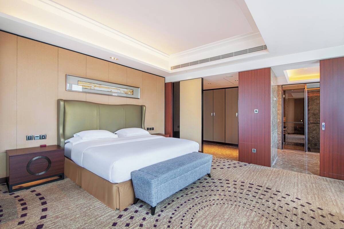 A hotel room with a large bed, a bench, a nightstand, a mirror, and a wardrobe.