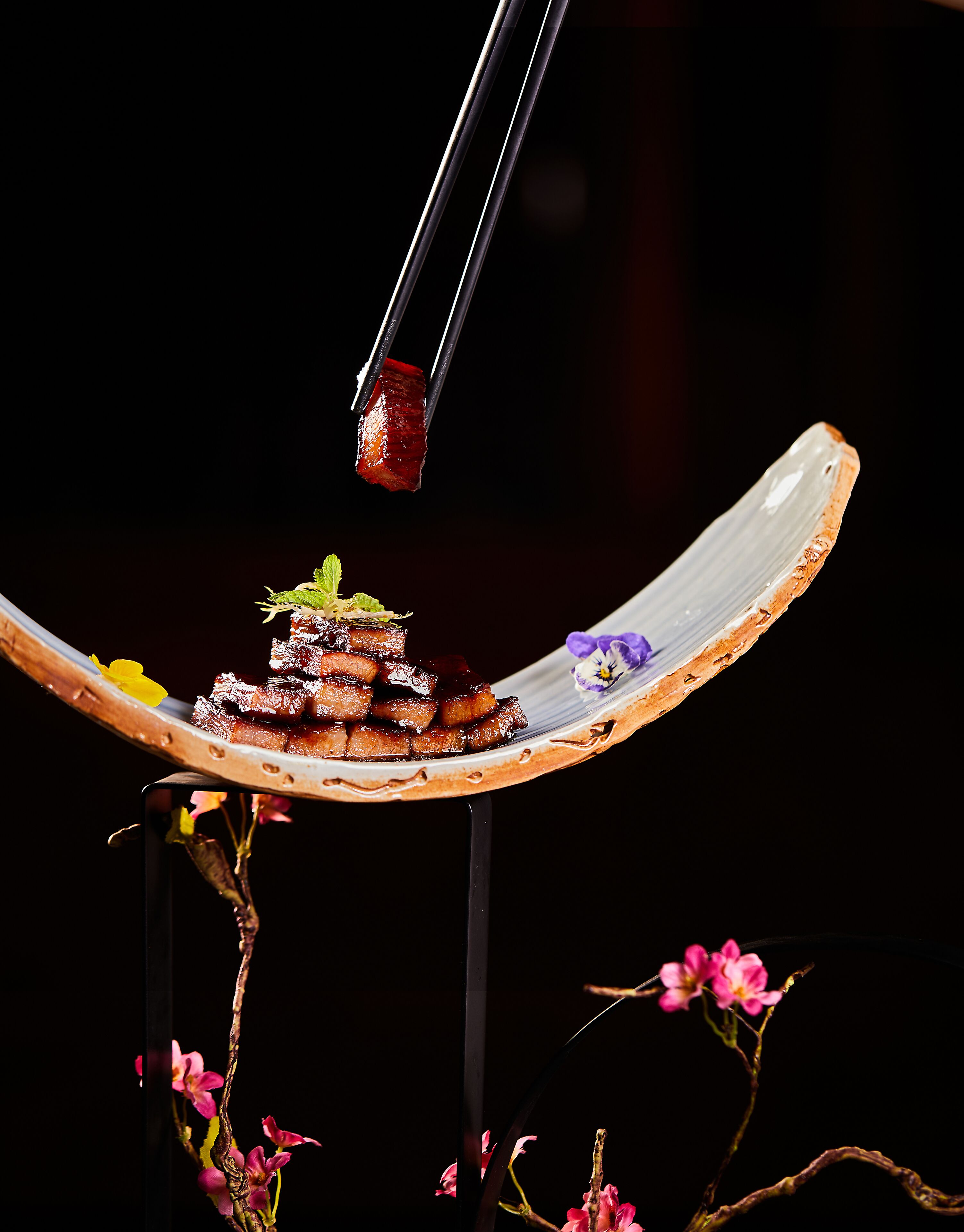 Un plato tradicional en una vajilla de cerámica con palillos, sobre un fondo oscuro con flores rosadas.