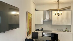 A modern kitchen with white cabinets, a dining table with chairs, and a chandelier. - Art Suites Athens (Athens)