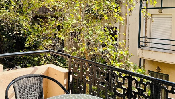 A balcony with a round table and chairs, surrounded by a metal railing and greenery. - Art Suites Athens (Athens)