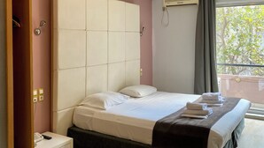 A bedroom with a large bed, a bedside table with a phone, a window with curtains, and an air conditioning unit. - Art Suites Athens (Athens)