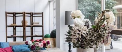 A room with a round glass table, a vase with flowers, a chandelier, and a sofa with cushions.
