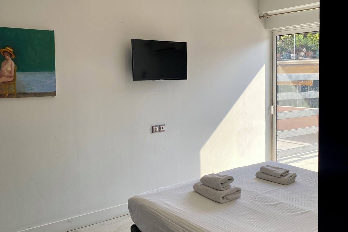 A modern hotel room with a large bed, a flat-screen TV mounted on the wall, and a painting above the bed.