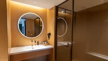 A modern bathroom with a wooden vanity, a round mirror, and a glass-enclosed shower.