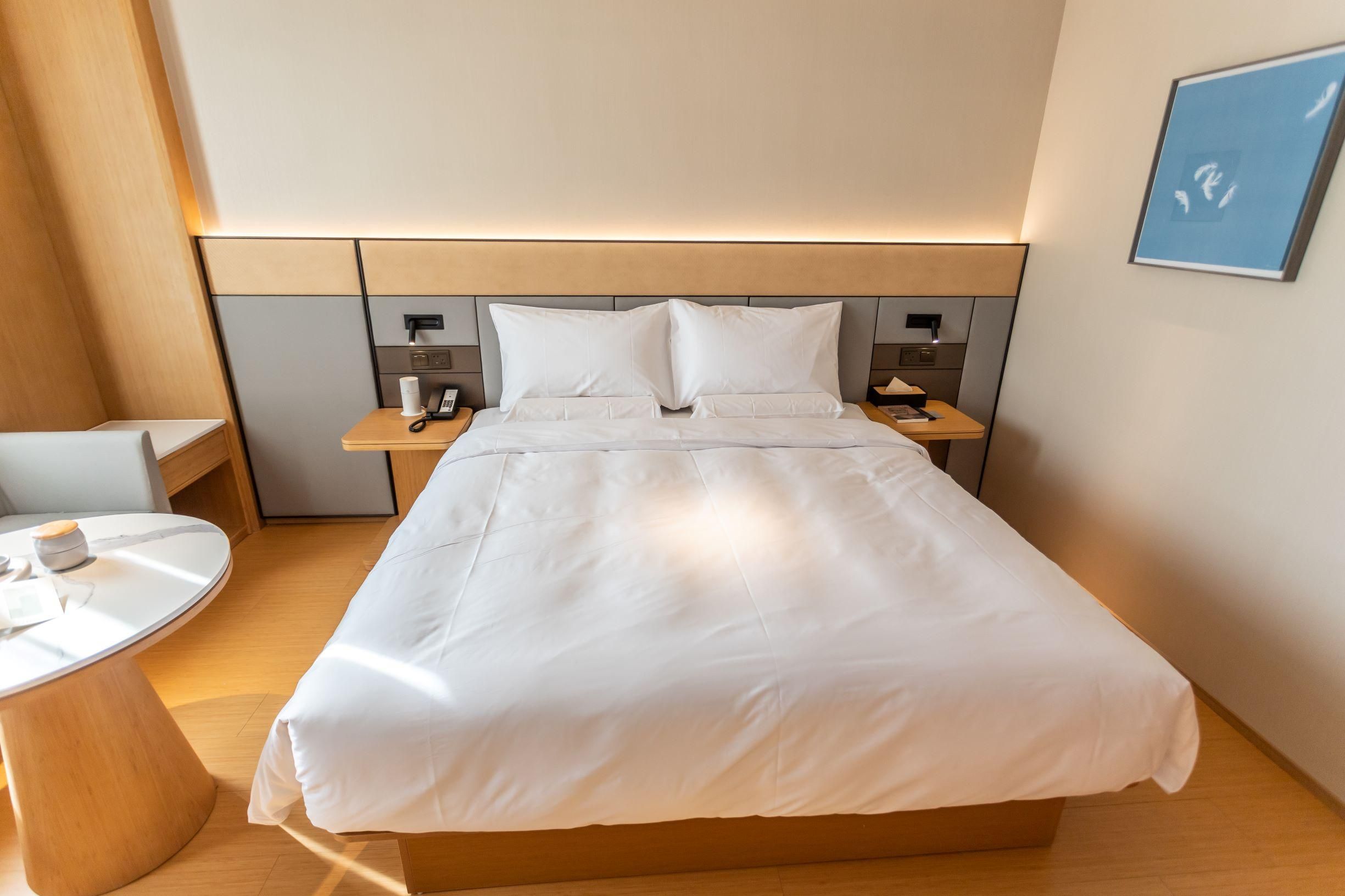Hotellihuone, jossa on suuri sänky, yöpöydät, pyöreä pöytä ja seinälle asennettu puhelin.
