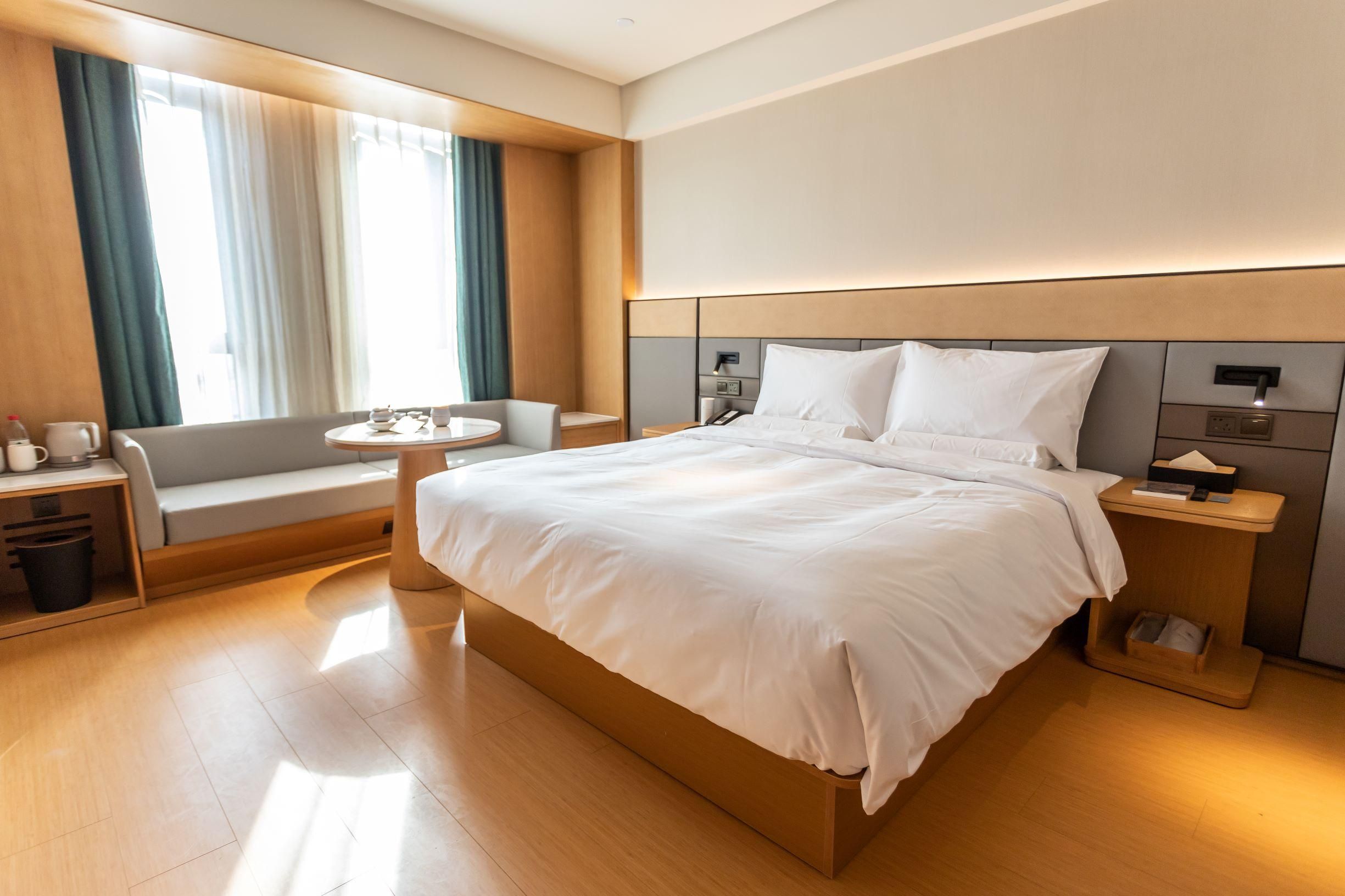A modern hotel room with a large bed, a seating area with a table, and a view of the outdoors.