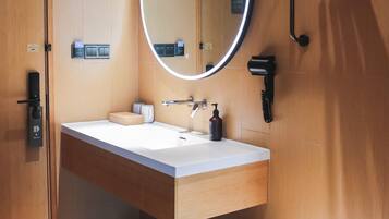Un baño moderno con tocador de madera, un espejo redondo con iluminación, un secador de pelo y un perchero para toallas.