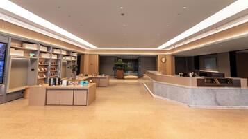 A modern hotel lobby with a reception desk, seating area, and a large plant in the center.