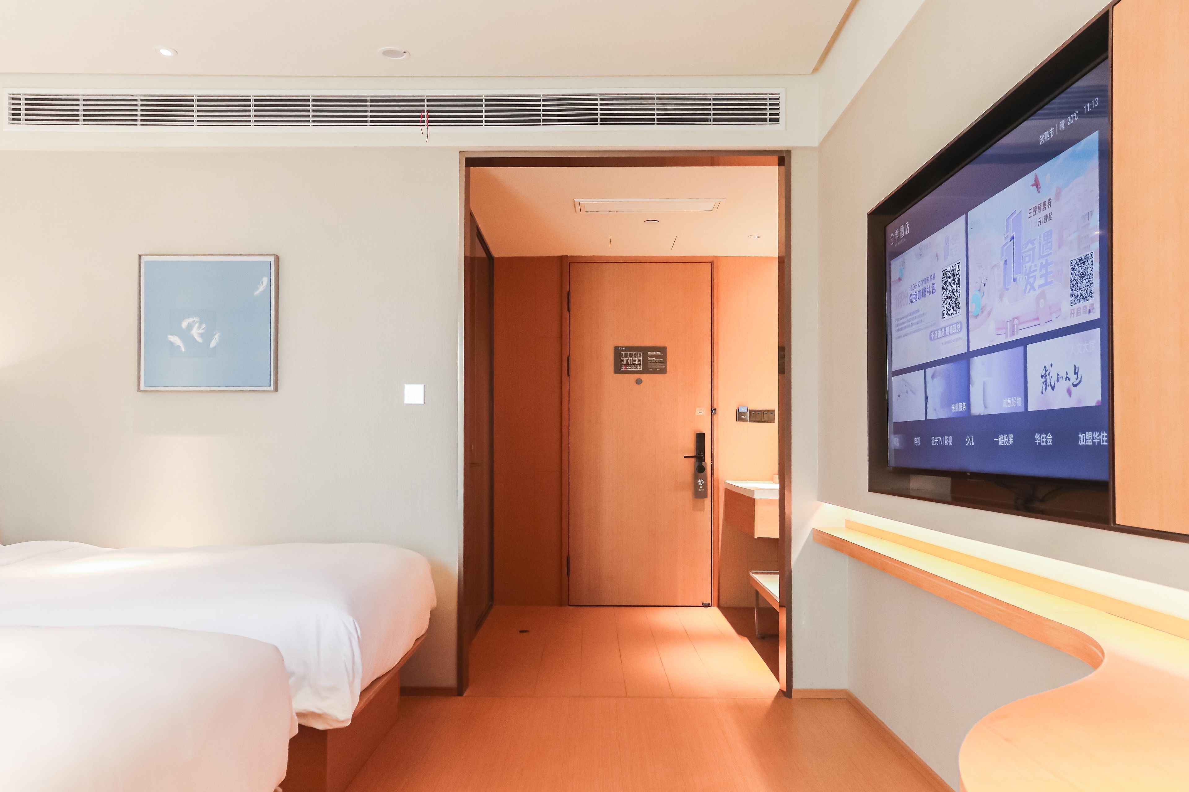 Habitación de hotel con dos camas, una pantalla de televisión mostrando información y una puerta que da a otra habitación.