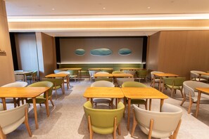 A conference room with multiple tables and chairs, a large screen, and a wall with three oval shapes. - Ji Hotel (Suzhou)
