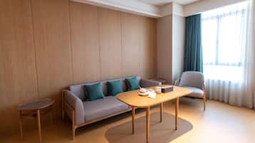 A modern hotel room with a sofa, a small table, a chair, and a window with curtains.