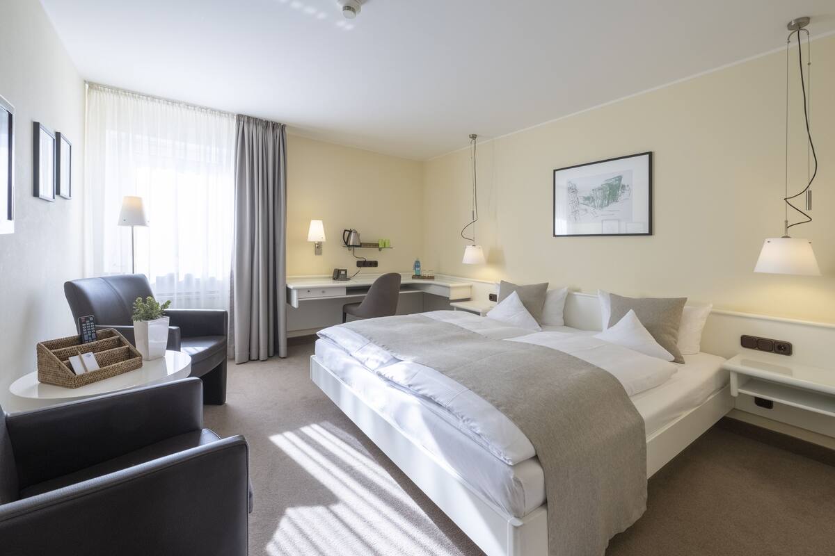 A hotel room with a bed, desk, chair, and a lamp.
