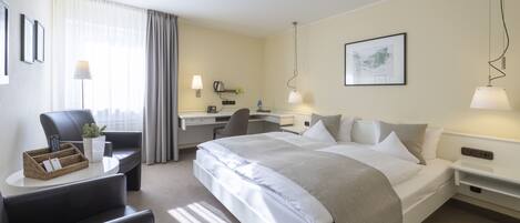 A hotel room with a bed, desk, chair, and a lamp.