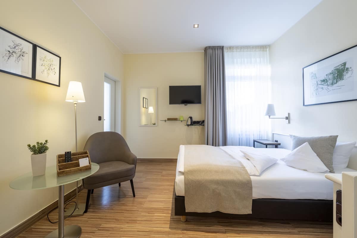 A hotel room with a bed, a desk, a chair, a TV, and artwork on the walls.