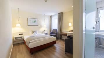 A hotel room with a bed, bedside tables, a chair, a desk, and a bathroom with a sink and mirror.