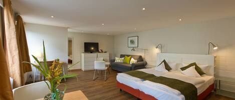 A modern hotel room with a large bed, a desk, a sofa, and a TV.