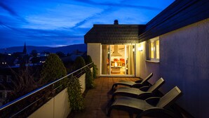 A balcony with outdoor seating and a view of the cityscape at dusk. - Hotel Deutscher Hof (Trier)