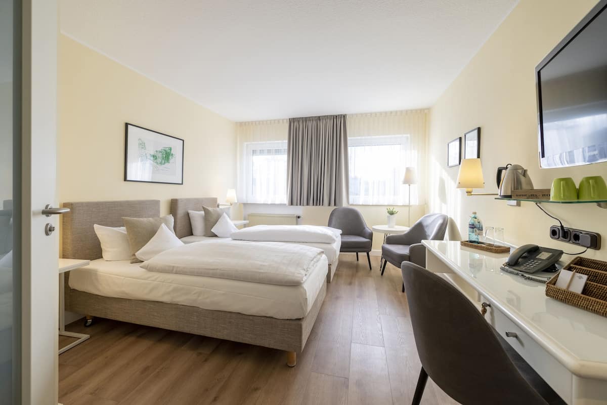 A hotel room with two beds, a desk, a chair, a television, and a window with curtains.