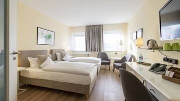 Ein Hotelzimmer mit zwei Betten, einem Schreibtisch, einem Stuhl, einem Fernseher und einem Fenster mit Vorhängen.