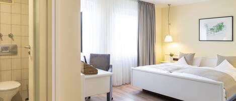 Una habitación de hotel con cama, escritorio, silla, inodoro y ducha.