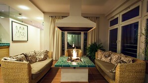 A living room with two wicker sofas, a central coffee table with a fire feature, and a large window with curtains. - Hotel Deutscher Hof (Trier)