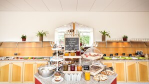 A breakfast buffet with various food items and beverages, a chalkboard menu, and potted plants. - Hotel Deutscher Hof (Trier)