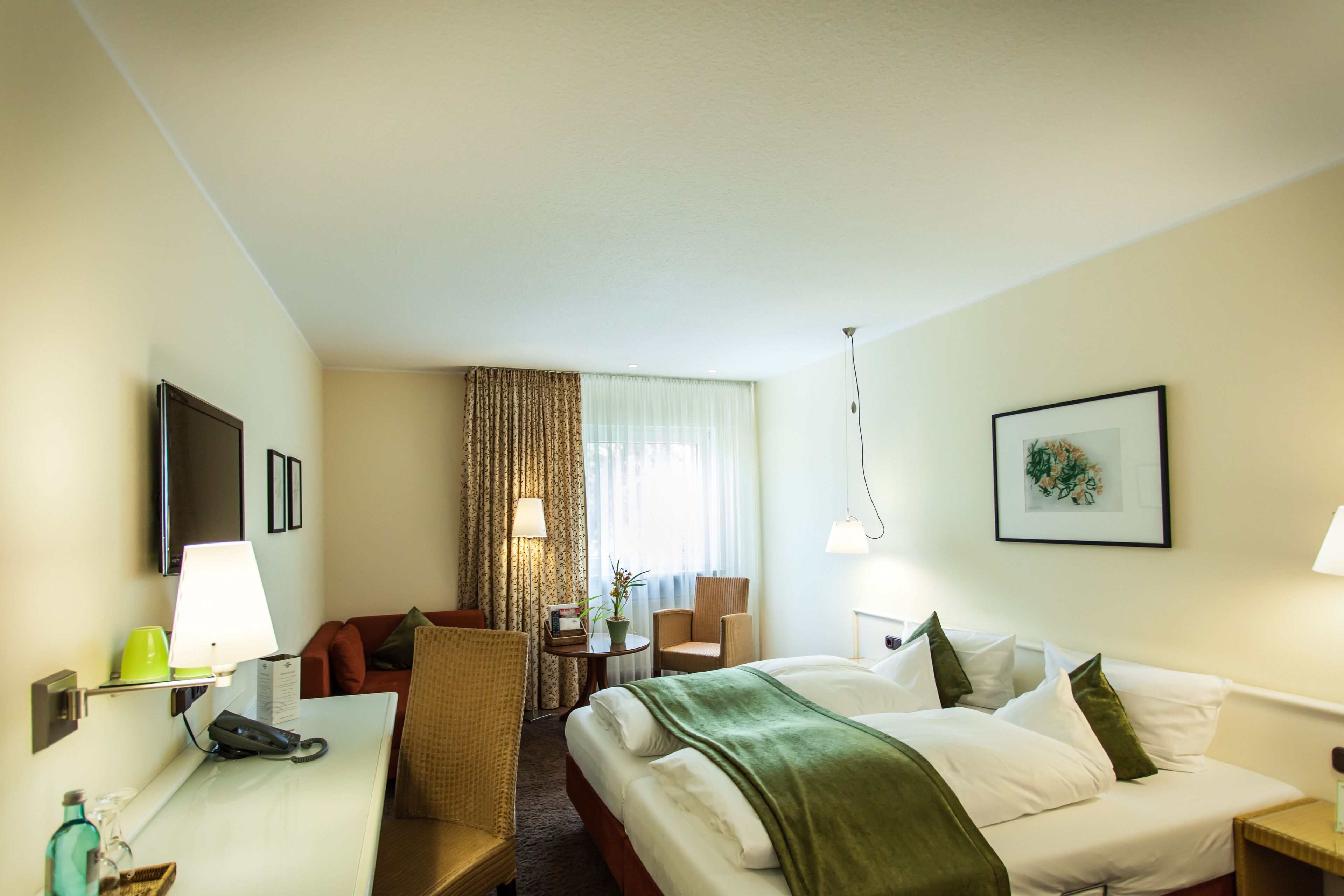 Habitación de hotel con cama, escritorio, silla, televisión y ventana con cortinas.