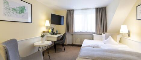 Ein Hotelzimmer mit Bett, Schreibtisch, Stuhl, Fernseher und einem Fenster mit Vorhängen.
