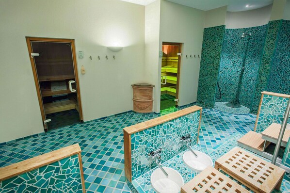 A bathroom with mosaic tile floors, wooden benches, and a shower area with a green mosaic wall. - Hotel Deutscher Hof (Trier)