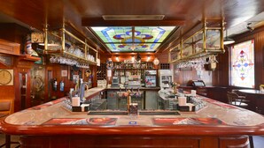 A bar with a wooden interior, a cash register, and a variety of bottles and glasses on shelves. -  Grand Astoria Hotel (Dubai)