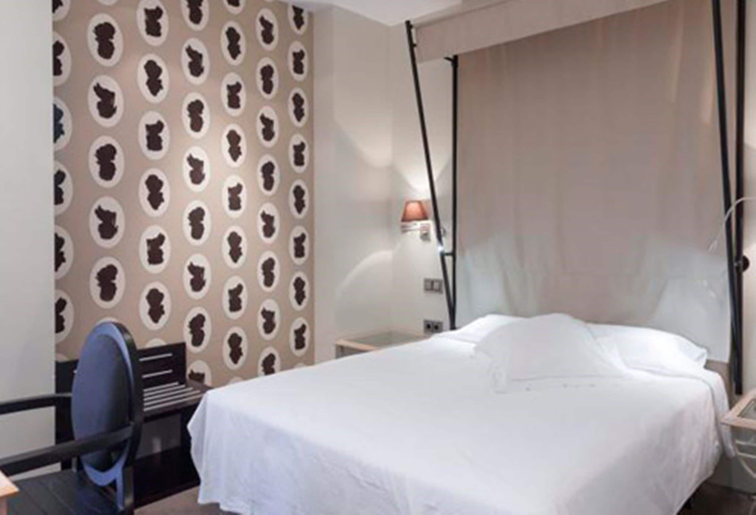 Habitació d'hotel amb llit, escriptori, cadira i paper tapet a la paret.