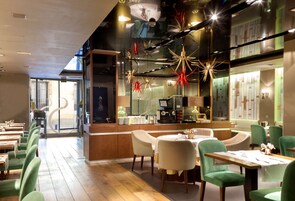 Un ristorante moderno con sedie verdi, tavoli di legno e un'area bar con bancone e sgabelli.