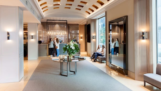 A modern hotel lobby with a high ceiling, a reception desk, a seating area, and a large mirror reflecting the interior. - Inhala Hotel Garden (Madrid)