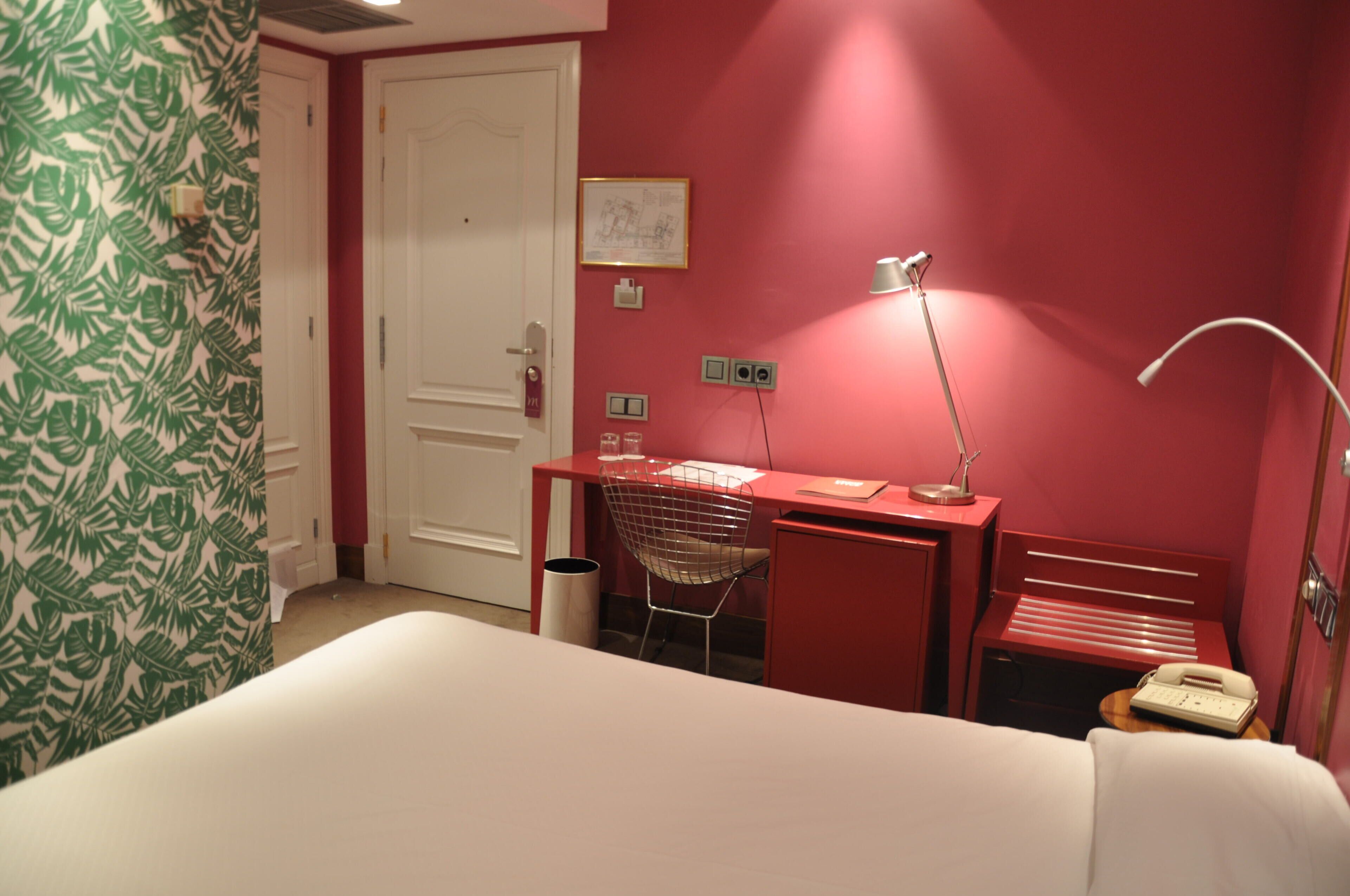 A hotel room with a bed, a desk with a chair, a lamp, and a telephone.