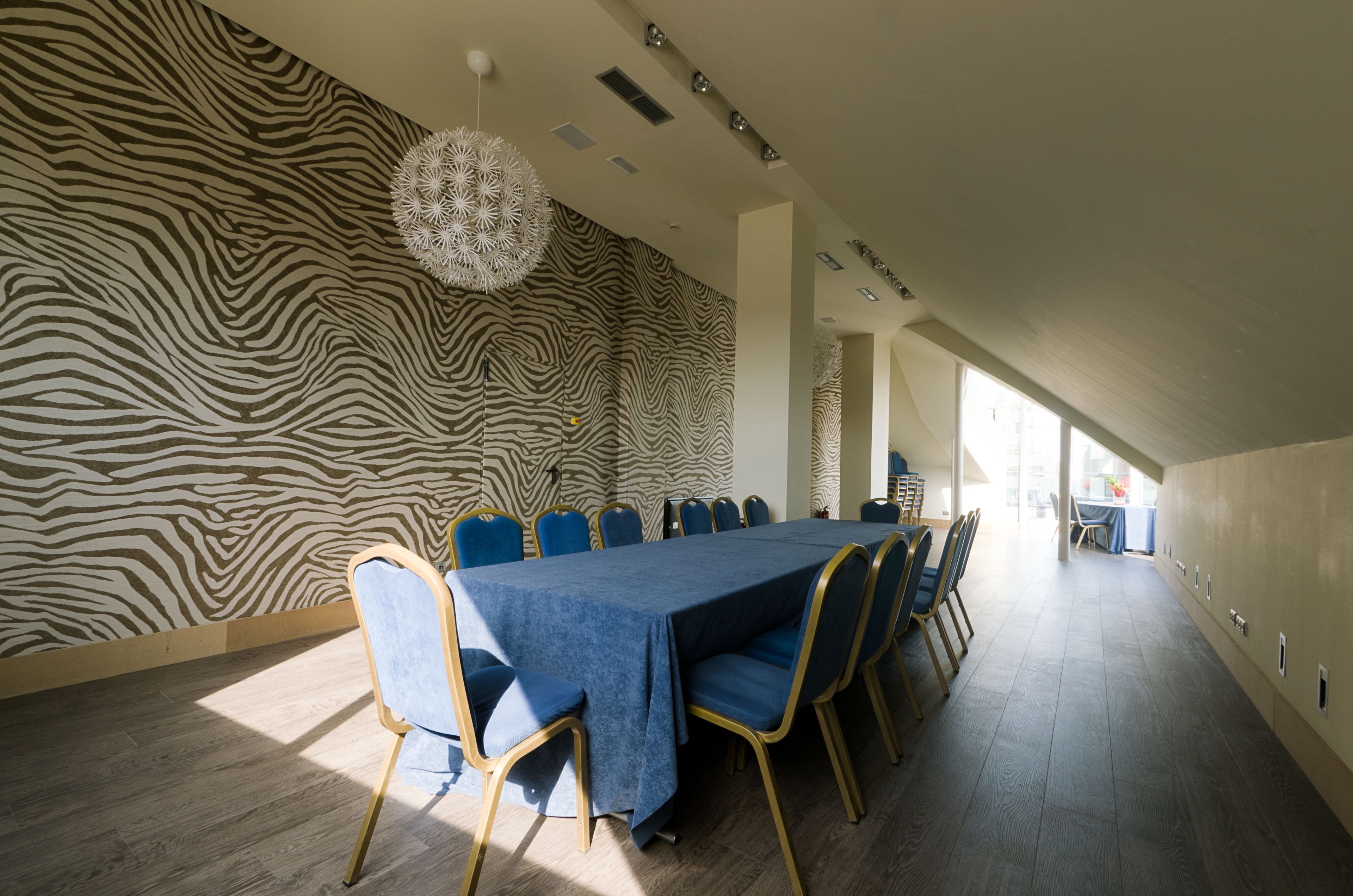 Ein Konferenzraum mit einer zebraartig gestreiften Wand, einem langen Tisch mit blauen Stühlen und einer hängenden Leuchte.