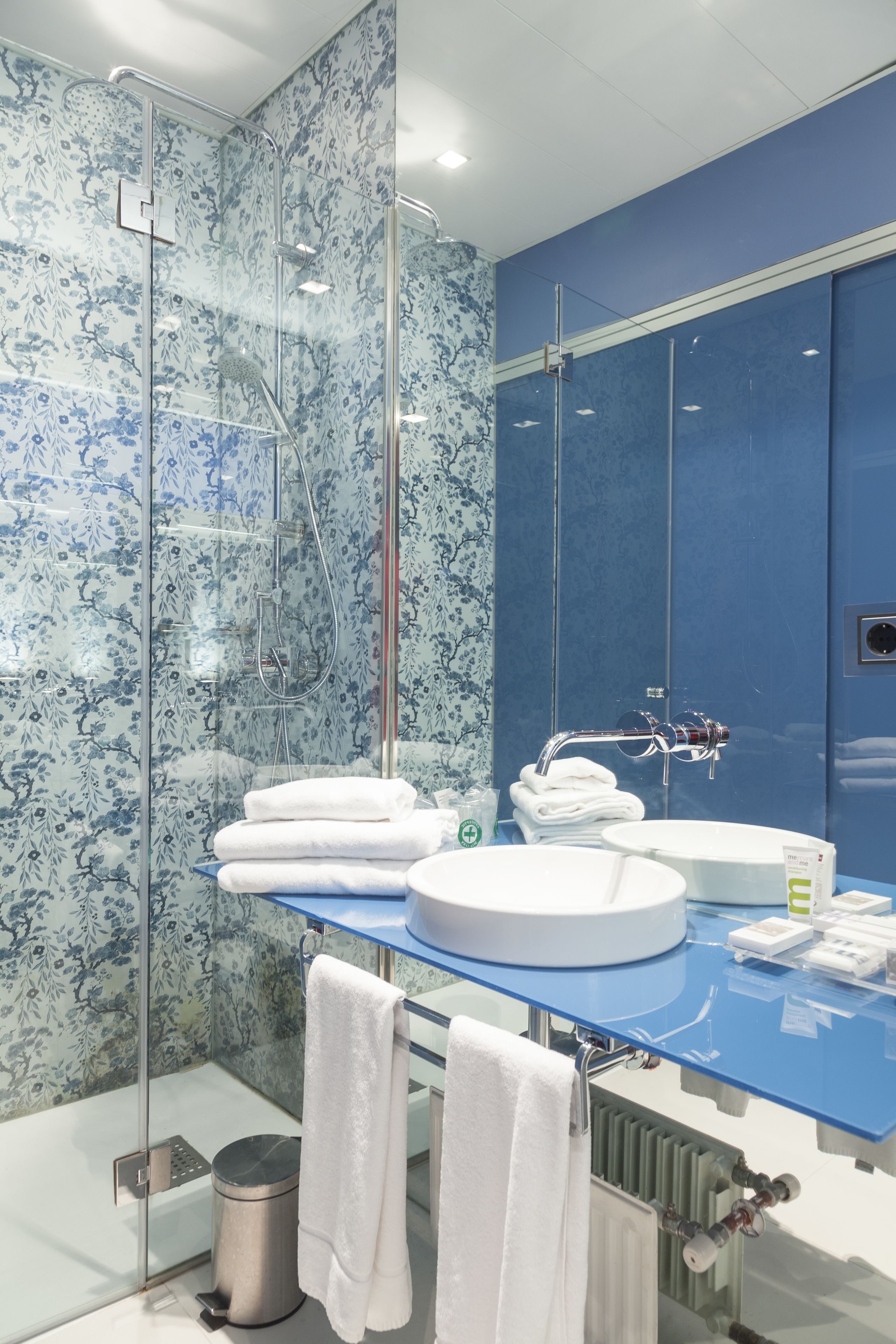 A modern bathroom with a glass shower enclosure, a blue vanity, and a large mirror.