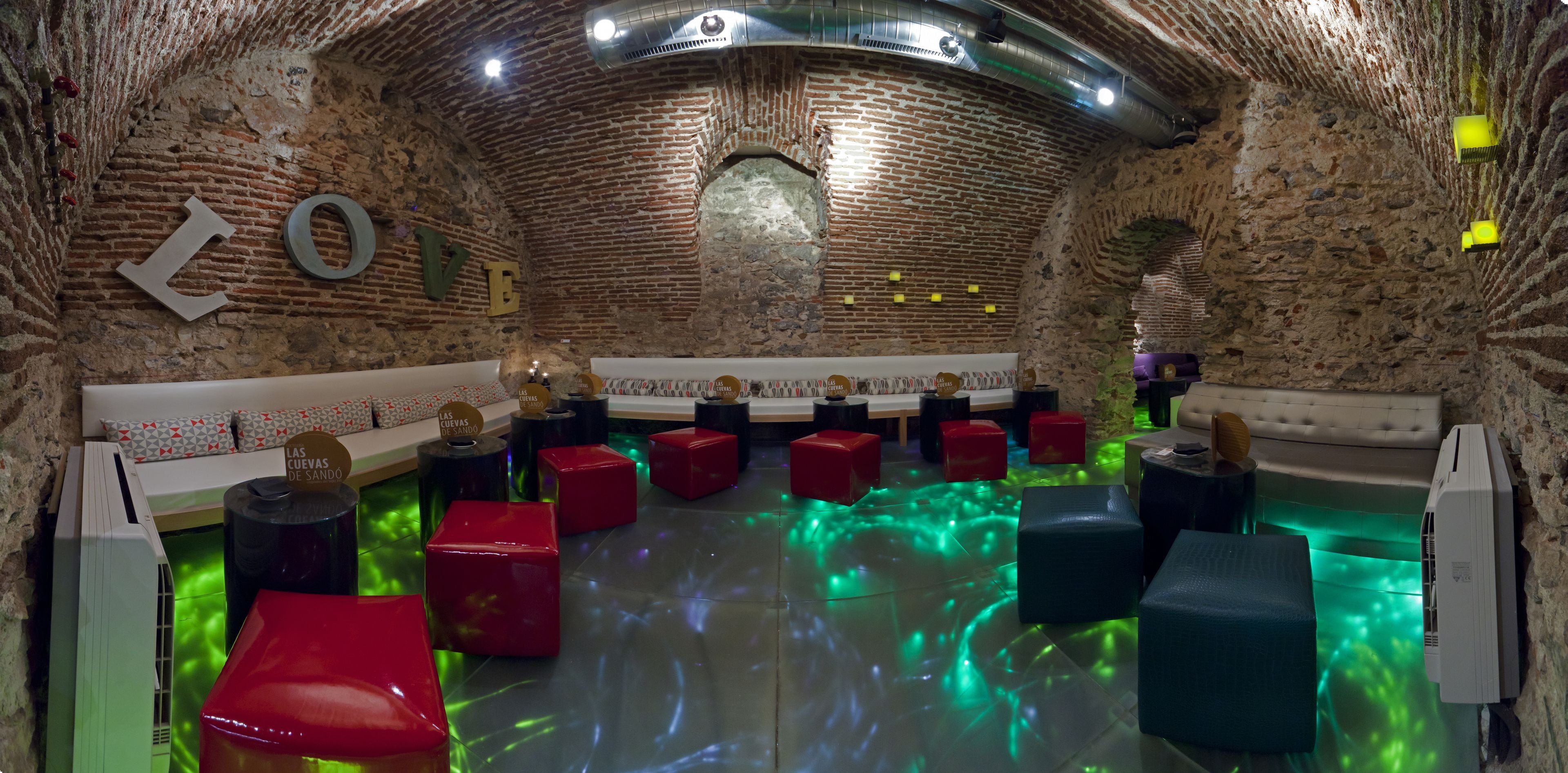 Una stanza della spa con parete in mattoni, una grande finestra ad arco e un’area relax con sgabelli rossi e blu.