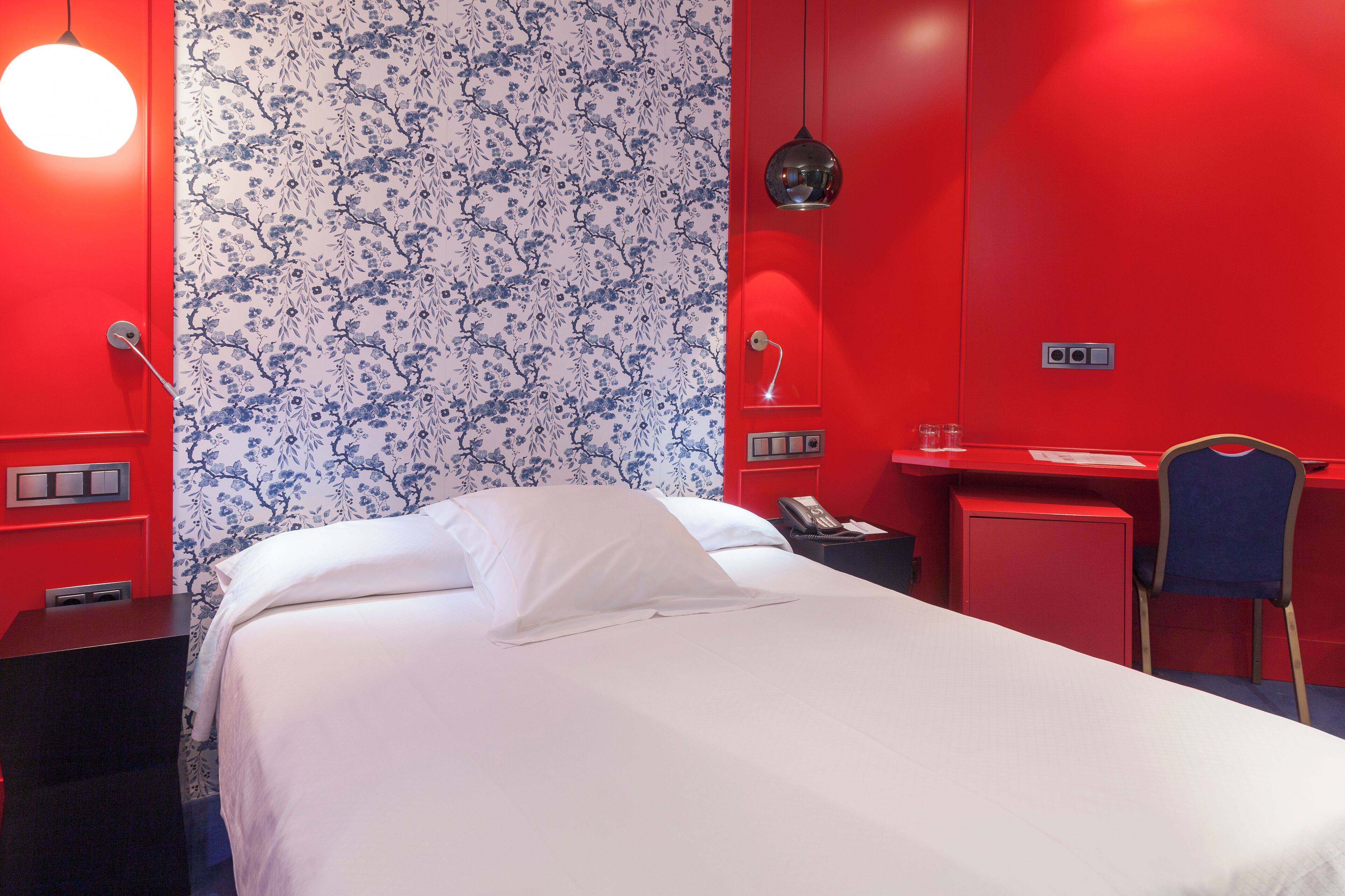 Habitación de hotel con cama, escritorio, silla y teléfono.
