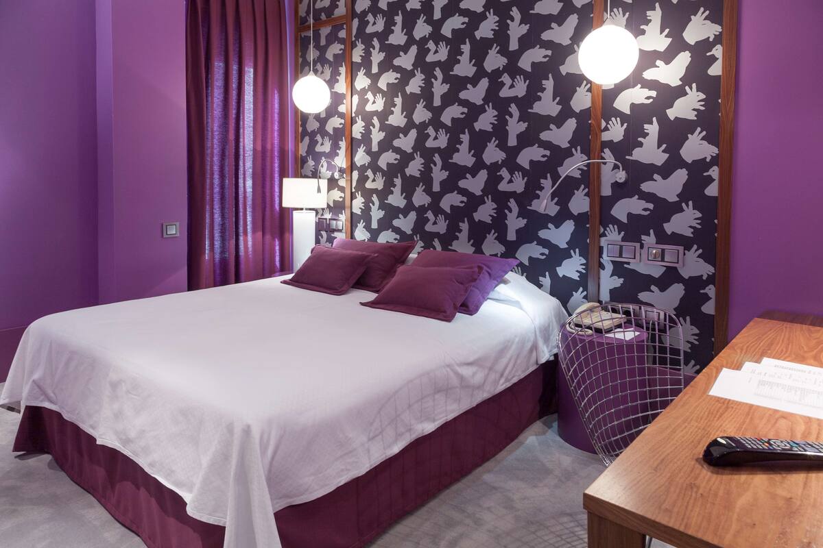 A bedroom with a bed, purple curtains, a nightstand, and a wall with a pattern of white animal silhouettes.