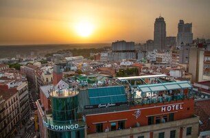 A hotel with a rooftop terrace and a view of the city skyline at sunset.