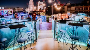 A rooftop bar with glass railings, bar stools, and a city view at night. - Inhala Hotel Garden (Madrid)